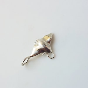 Puede incluir: Un colgante de plata en forma de mantarraya. El colgante tiene forma de mantarraya con un bucle en la parte superior para sujetarlo a una cadena o pulsera.