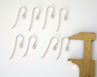 May include: Eight silver earring hooks, measuring approximately 1 inch in length, are displayed on a white surface. A ruler is used to measure the hooks.
