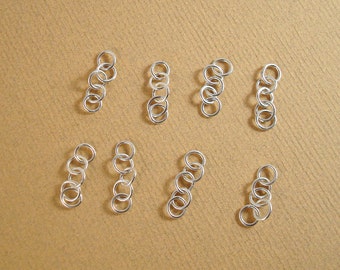Könnte beinhalten: Nahaufnahme von mehreren kleinen, silberfarbenen Sprungringen, die auf einer hellbraunen Oberfläche angeordnet sind. Jeder Ring ist mit anderen verbunden und bildet kleine Ketten. Die Ringe scheinen aus Metall zu sein.