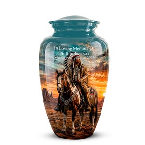 Peut inclure: Une urne funéraire en métal bleu sarcelle ornée d'une scène imprimée représentant une personne en tenue traditionnelle amérindienne à cheval dans un paysage désertique au coucher du soleil. Le texte indique In Loving Memory Of Phillips Jackson Mar/08/1991-Jan/10/2025.