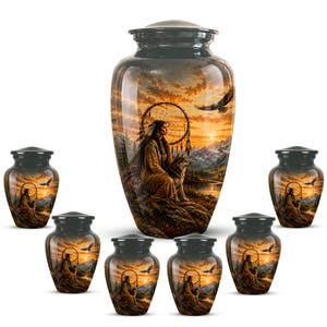May include: A collection of seven dark-toned metal cremation urns featuring a printed scene of a person sitting with a wolf near a dreamcatcher against a sunset mountain landscape. Each urn has a matching lid and a smooth, polished finish.