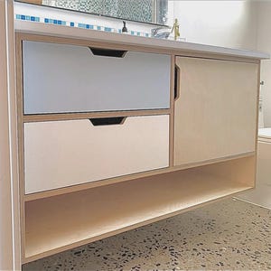 May include: A wall-mounted bathroom vanity cabinet constructed from light-colored plywood. The unit features two stacked drawers with cut-out handles, one light blue and one white, alongside a single cabinet door and an open bottom shelf.