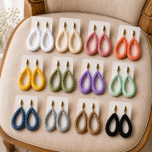 Può includere: Dodici paia di orecchini a forma di goccia con filo all'uncinetto in vari colori, tra cui bianco, crema, rosa, arancione, giallo, verde, viola, menta, blu, grigio, beige e nero, fissati su un perno in metallo color oro.