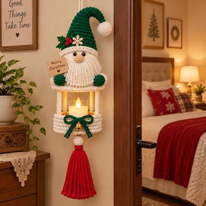 Op de afbeelding: Een gehaakte wandhanger met een kabouter met een groene muts, witte baard en een houten bordje met de tekst Merry Christmas. Onder de kabouter bevindt zich een ronde houder met een witte led-kaars, een groene strik, een gouden bel en een rode kwast.