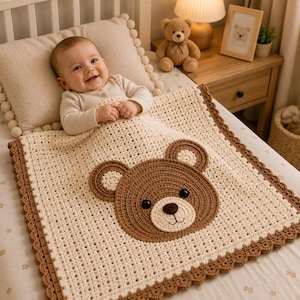 Può includere: Una coperta per neonati all'uncinetto color crema con un grande muso d'orso marrone al centro, occhi scuri e naso ricamato. La coperta presenta un bordo decorativo smerlato marrone e un motivo a maglia aperta su tutta la superficie.