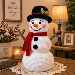 May include: A white crocheted snowman doll featuring a black hat with green holly leaves and red berries, a bright red scarf, an orange carrot-shaped nose, two black circular buttons on its chest, and brown twig-like arms made of yarn.