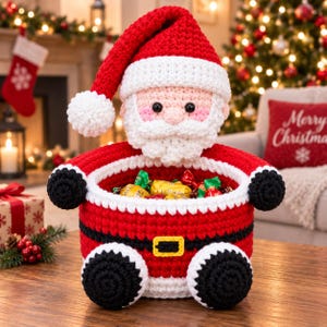 Könnte beinhalten: Ein gehäkelter Weihnachtsmann-Korb mit einer rot-weißen Mütze, einem weißen Bart und einem Gesicht mit schwarzen Augen. Der Korbkörper ist rot mit einem schwarzen Gürtel und einer gelben Schnalle, akzentuiert durch gehäkelte Füße und Arme.