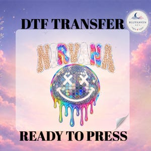 May include: A DTF transfer sheet featuring the word NIRVANA in a mix of leopard print, checkerboard, and tie-dye patterns. Below the text is a disco ball smiley face with X-shaped eyes and colorful paint-like drips in rainbow hues.