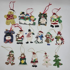 May include: A collection of fourteen assorted Christmas ornaments featuring figures including gingerbread people, snowmen, Santa Claus, penguins, bears, angels, and Christmas trees, each with a hanging string for display on a holiday tree.