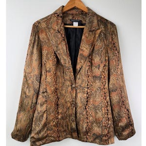 May include: A long-sleeve blazer featuring a brown and black snakeskin pattern. The garment has a notched lapel, a black interior lining, and two front buttons for closure. The fabric has a subtle sheen, and the overall design includes structured shoulders and a tailored fit.
