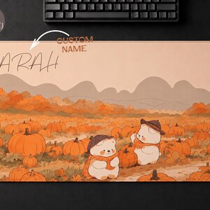 Op de afbeelding: Een rechthoekige bureaumat met een herfstachtige pompoenveldillustratie met twee cartoonberen die hoeden en sjaals dragen. De tekst SARAH staat in de linkerbovenhoek gedrukt, met de woorden CUSTOM NAME boven de naam.