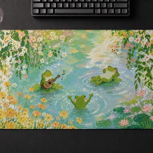 May include: A rectangular desk mat featuring an illustration of three green frogs in a pond surrounded by yellow and white flowers. One frog plays a guitar, another relaxes on a lily pad, and the third swims in the water with arms raised.