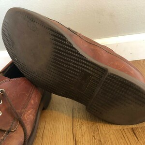 May include: A pair of brown leather shoes with laces. The shoes have a textured sole and are worn.