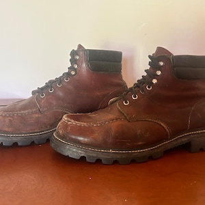 以下が含まれることがあります： 黒の革のアクセントが付いた茶色の革製のワークブーツのペア。ブーツはレースアップで厚底です。