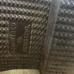 May include: Close-up of the bottom of a brown leather boot with a black rubber sole. The sole is textured and has the words "Armored" and "Oil Resisting" printed on it.