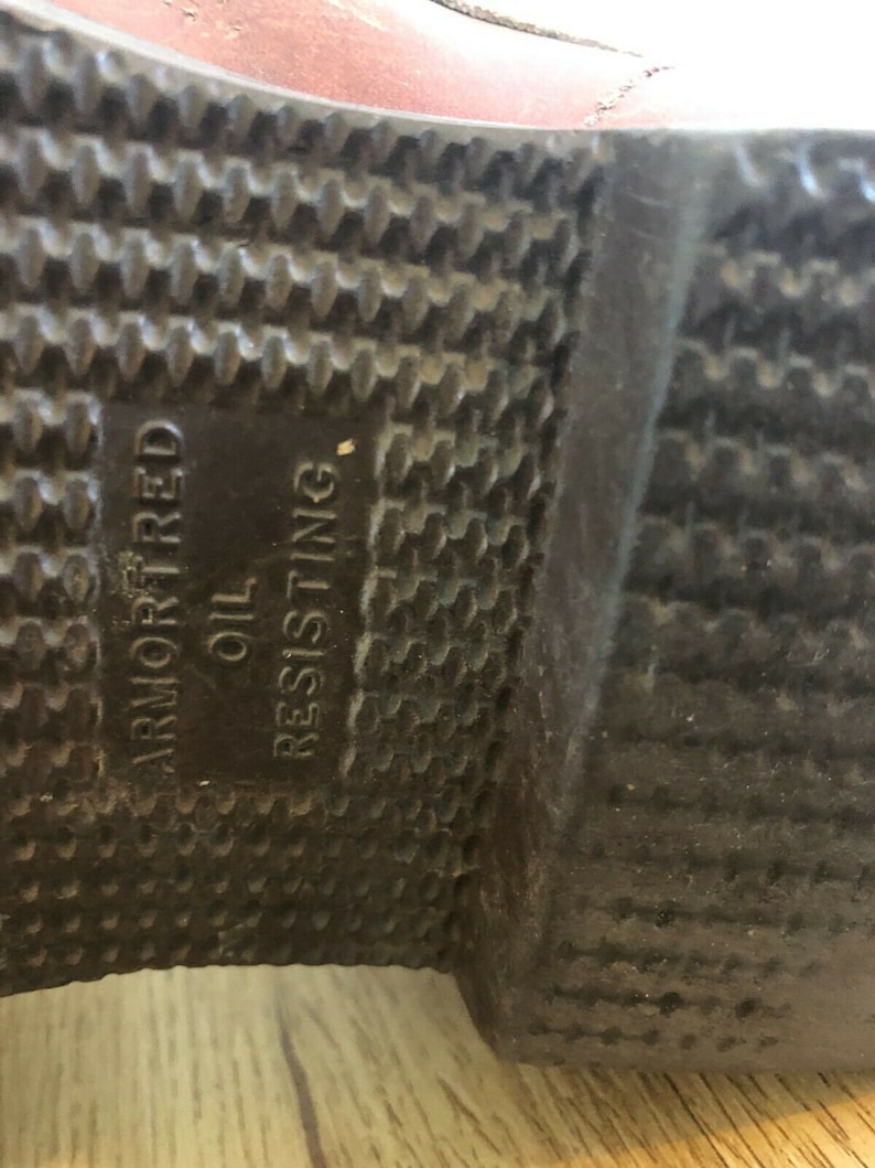 May include: Close-up of the bottom of a brown leather boot with a black rubber sole. The sole is textured and has the words "Armored" and "Oil Resisting" printed on it.