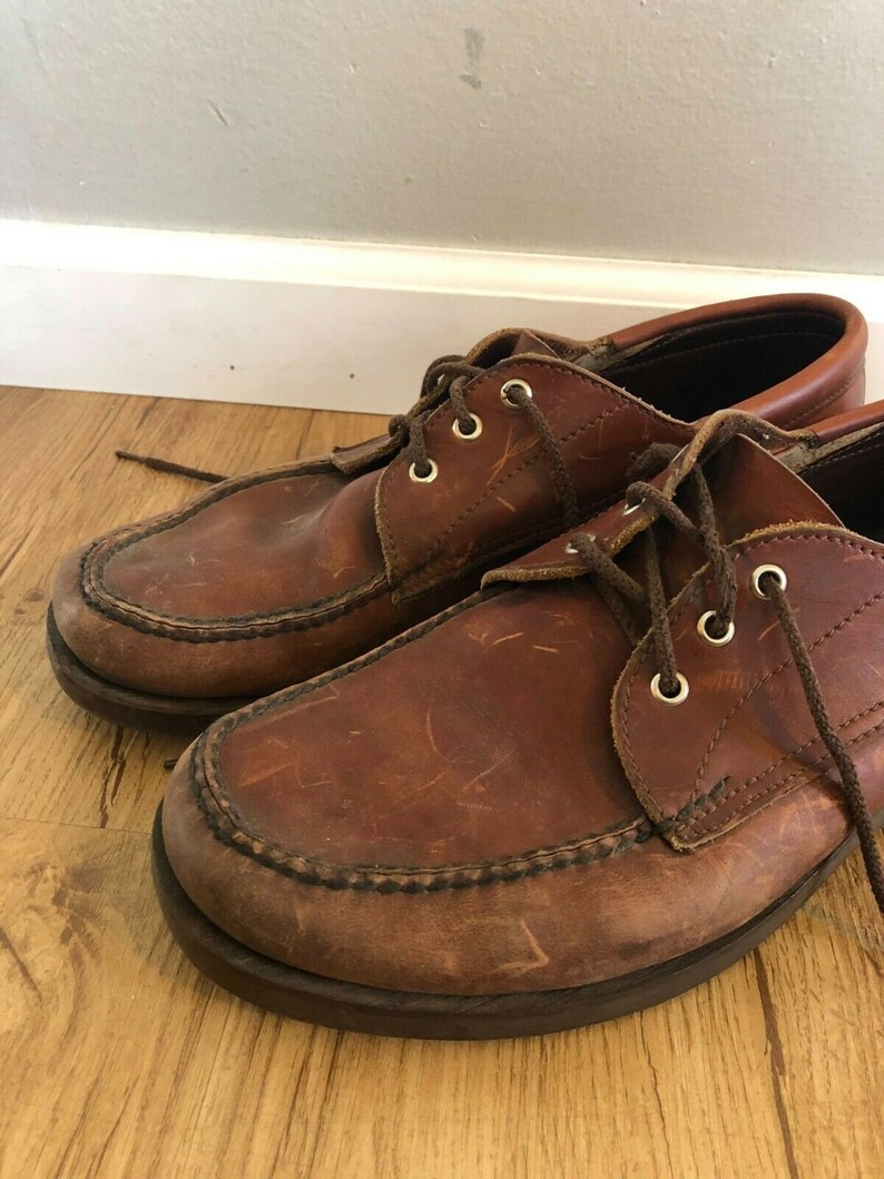 May include: A pair of brown leather lace-up shoes with a moc toe design. The shoes have a worn look and are made of a durable material.