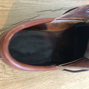 May include: Close-up view of the inside of a brown leather shoe. The shoe is unlaced and the inside is lined with a dark brown fabric.