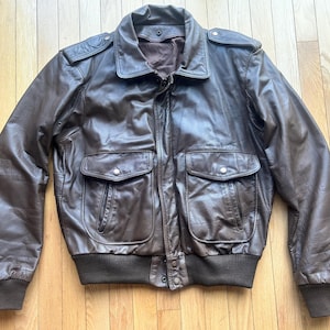 May include: A brown leather bomber jacket with a zipper closure, two large pockets, and a ribbed knit collar, cuffs, and waistband.