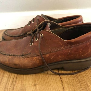 May include: A pair of brown leather lace-up shoes with a moc toe design. The shoes have a thick sole and a brown leather laces.