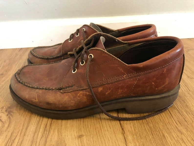 May include: A pair of brown leather lace-up shoes with a moc toe design. The shoes have a thick sole and a brown leather laces.