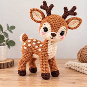 May include: A crocheted deer toy featuring a brown body with white spots on its back, a cream-colored chest, and dark brown antlers. The deer has large black eyes with long eyelashes, pink cheeks, and dark brown hooves on its four legs.