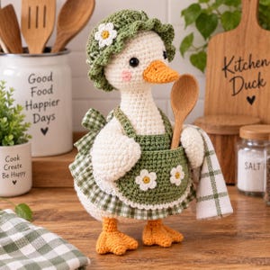 Puede incluir: Una figura de pato tejida a ganchillo con un gorro verde con una flor blanca, un delantal de cuadros verdes con dos flores blancas y pies naranjas. El pato sostiene una pequeña cuchara de madera y tiene una toalla de cuadros verdes y blancos.