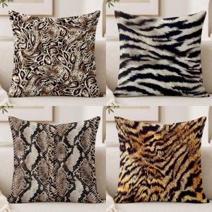 May include: A set of four square throw pillows featuring distinct animal print patterns. The top left displays a brown and black leopard print, the top right a black and white zebra stripe, the bottom left a brown and black snakeskin, and the bottom right a gold and black tiger stripe.