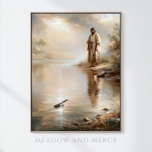 May include: A framed wall art print titled Meadow and Mercy, depicting a figure in a light-colored robe standing on a riverbank. An axe head rests in the shallow water, reflecting the soft, warm light of a cloudy sky over the calm river landscape.