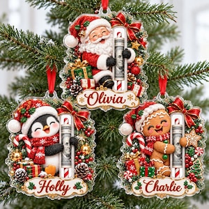 May include: Three clear acrylic Christmas ornaments featuring Santa Claus, a penguin, and a gingerbread person. Each ornament holds a rolled-up 100 dollar bill in a central tube, decorated with red bows, pine cones, and names Olivia, Holly, and Charlie.
