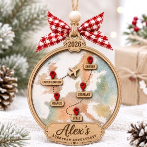 May include: A round wooden ornament featuring a map of Europe with red location pins labeled United Kingdom, Sweden, Germany, France, and Italy. A small wooden airplane follows a dotted path. The text reads 2026 and Alex's European Adventures.