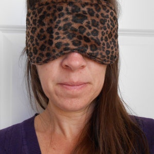 May include: A person wearing a brown and black leopard print sleep mask.
