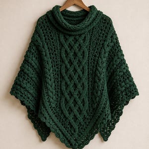 May include: A dark forest green knit poncho featuring a prominent central cable knit pattern, a high cowl neckline, and an openwork stitch design throughout the body. The garment is finished with a single decorative tassel at the bottom point.