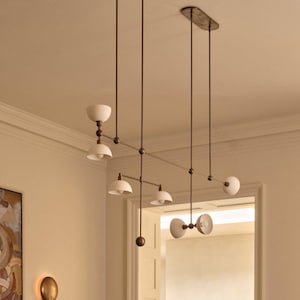 May include: A linear chandelier featuring a dark bronze metal frame with multiple adjustable arms and white dome-shaped shades. The fixture is suspended from the ceiling by two thin rods and includes spherical accents at the joints of the structure.