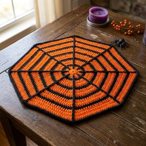 May include: A crocheted doily featuring an octagonal spider web pattern in alternating bands of bright orange and black yarn. The textile piece is flat with a central point radiating outward to the edges, creating a geometric web design.