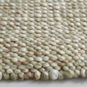 May include: A textured rug composed of numerous small, rounded, felted wool balls in a variegated color palette of soft sage green, creamy off-white, and muted beige tones, creating a dense, tactile surface with a consistent, repeating pattern.