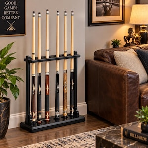 May include: A black wooden floor rack holding six pool cues. The cues feature light wood shafts and varied dark wood butts with decorative diamond inlays. The rack has a rectangular base and a top support bar with six circular cutouts for the cues.