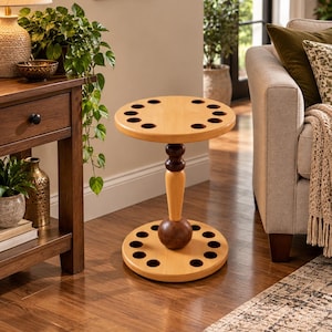 May include: A round wooden stand featuring a light-toned top and base, each with eight circular cutouts. The central support column consists of a light-toned tapered section flanked by two dark brown spherical and cylindrical wooden accents.