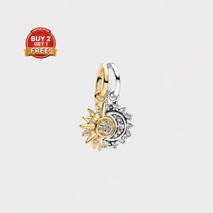 May include: A two-tone metal charm featuring a gold-colored sun and a silver-colored moon, both adorned with small clear stones. The sun has radiating rays, while the moon is crescent-shaped with a textured surface, both attached to a metal ring.