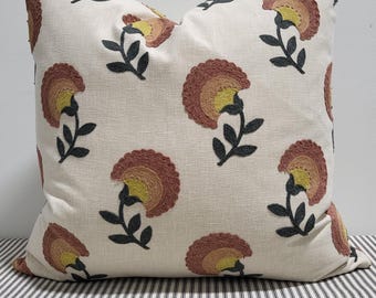 Könnte beinhalten: Ein quadratisches Zierkissen mit cremeweißem Grund und einem sich wiederholenden gestickten Blumenmuster. Die Blüten bestehen aus konzentrischen Halbkreisen in Terrakotta und Senfgelb mit dunkelgrauen Stielen und Blättern.