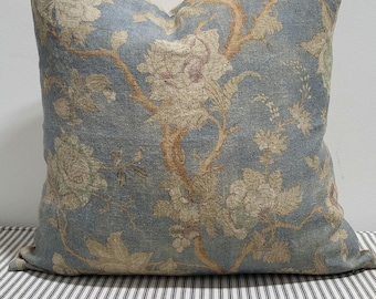 Könnte beinhalten: Ein quadratisches Zierkissen mit einem staubblauen Stoffgrund und einem gewebten Blumenmuster in Beige-, Creme- und gedeckten Brauntönen. Das Design zeigt komplexe botanische Motive, darunter große Blüten und geschwungene Zweige auf der Oberfläche.