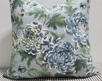 Könnte beinhalten: Ein quadratisches Zierkissen mit hellblauem Hintergrund und einem sich wiederholenden botanischen Muster aus großen, geschichteten Chrysanthemenblüten in Blau-, Weiß- und Grüntönen, ergänzt durch detaillierte grüne Blätter und Stängel.