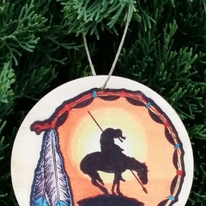 May include: Wooden ornament featuring a Native American on horseback silhouette against a sunset backdrop. The design includes a feather and a decorative border. The ornament is suspended by a string, perfect for holiday decor.