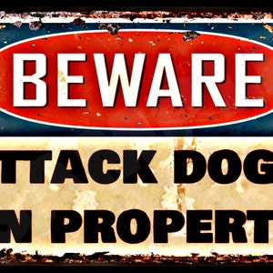 May include: A rectangular metal sign with a distressed, rusty appearance. The sign features the words "BEWARE" in white on a red and blue oval, above "ATTACK DOGS ON PROPERTY" in black, all against a yellowed background.