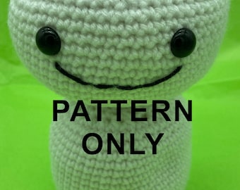 Pode incluir: Boneca de crochê cinza claro com cabeça e corpo redondos, olhos de botão pretos e um sorriso costurado. O texto "PATTERN ONLY" está impresso no corpo. O fundo é verde brilhante.