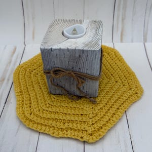 Puede incluir: Un portavelas de madera gris con una vela falsa se encuentra sobre un posavasos cuadrado de ganchillo amarillo. El portavelas está envuelto con hilo. El posavasos está hecho de un hilo grueso y texturizado.