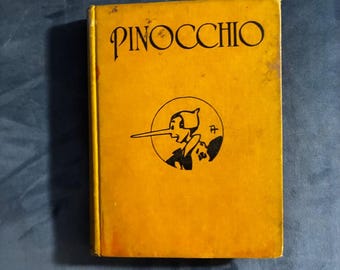 Puede incluir: Un libro de tapa dura con una cubierta de color amarillo brillante que presenta el título PINOCCHIO en letras negras en la parte superior. Debajo del título hay un dibujo lineal circular en negro del personaje Pinocchio de perfil.