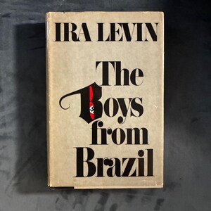 May include: A hardcover book titled The Boys from Brazil by Ira Levin. The cover is a light tan color with bold black text. The letter B in the word Boys is stylized in black with a small red accent containing a tiny black swastika symbol.