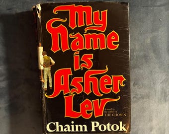 Puede incluir: Un libro de tapa dura titulado My Name is Asher Lev de Chaim Potok. La sobrecubierta negra presenta letras llamativas y estilizadas en rojo y amarillo. Una ilustración de una persona de pie frente a un caballete es visible en el lado izquierdo.