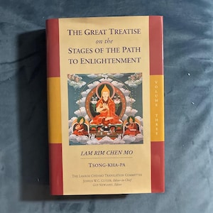 May include: A book titled The Great Treatise on the Stages of the Path to Enlightenment, Volume Three, by Tsong-kha-pa. The cover features a central illustration of a seated figure in orange robes, with red and yellow borders and black text.